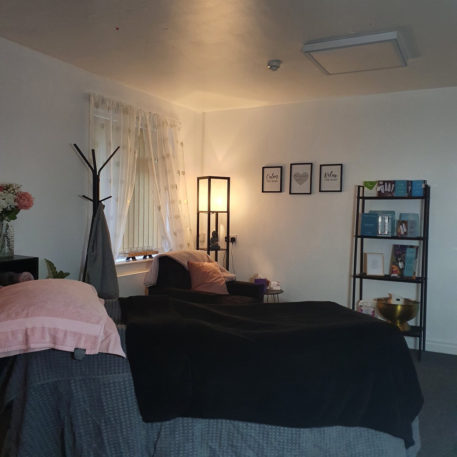 Lisa’s treatment room in warm lamp light, with the massage bed made up and an armchair beside it