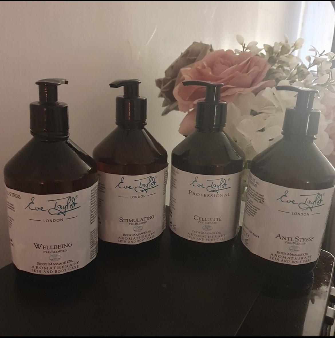 Four bottles of Eve Taylor massage oil with flowers behind