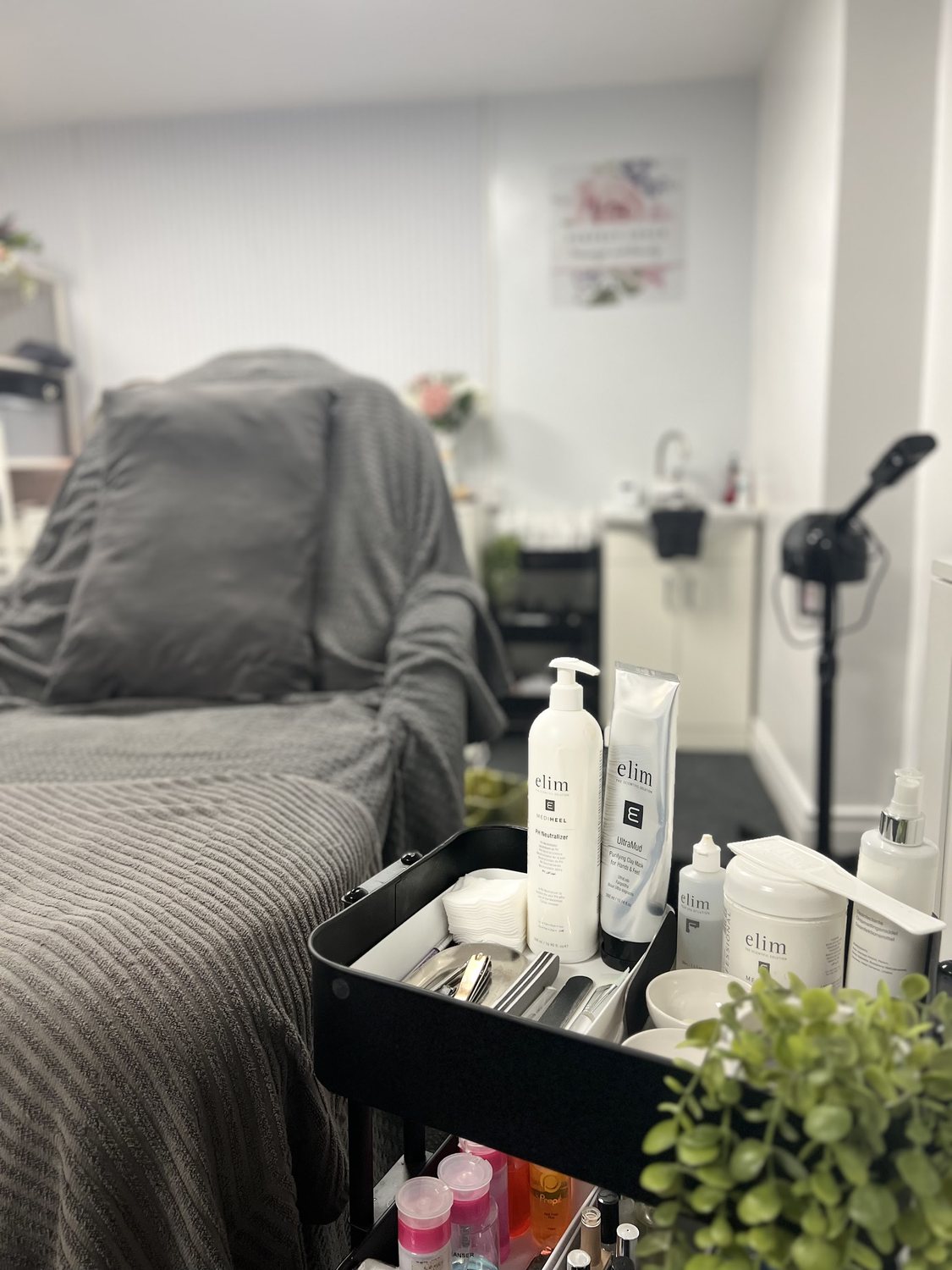 The treatment bed with a grey blanket, a product trolley and a plant